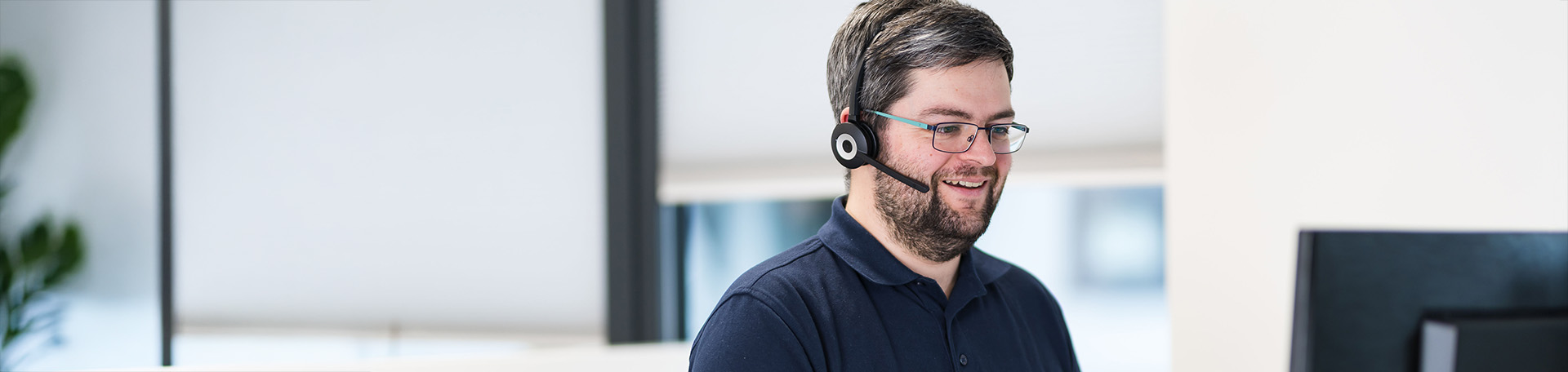 Person mit Headset arbeitet an einem Computer in einem hellen Büro.